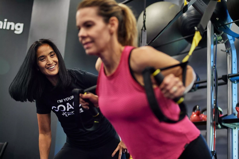 Trainer assisting woman with TRX suspension training in the gym